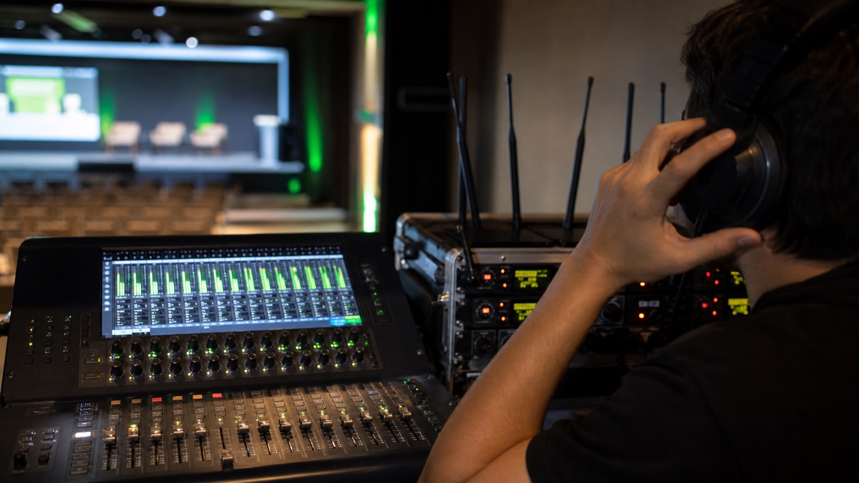 Técnico a monitorizar uma mesa de mistura e microfones sem fios num evento