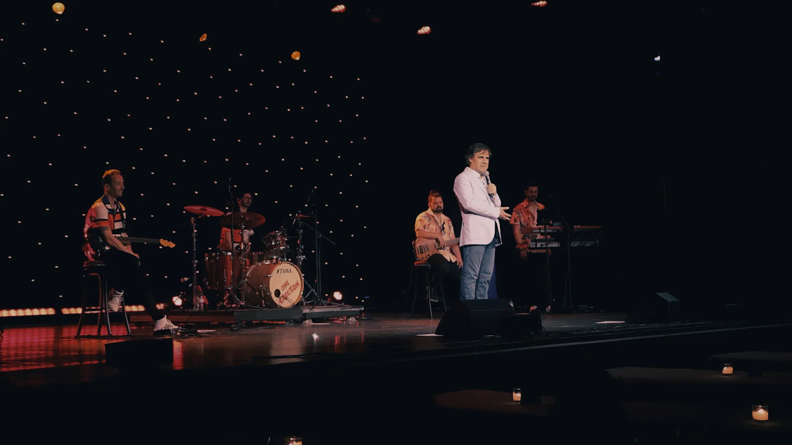 Plano geral de uma atuação em palco, com banda e iluminação